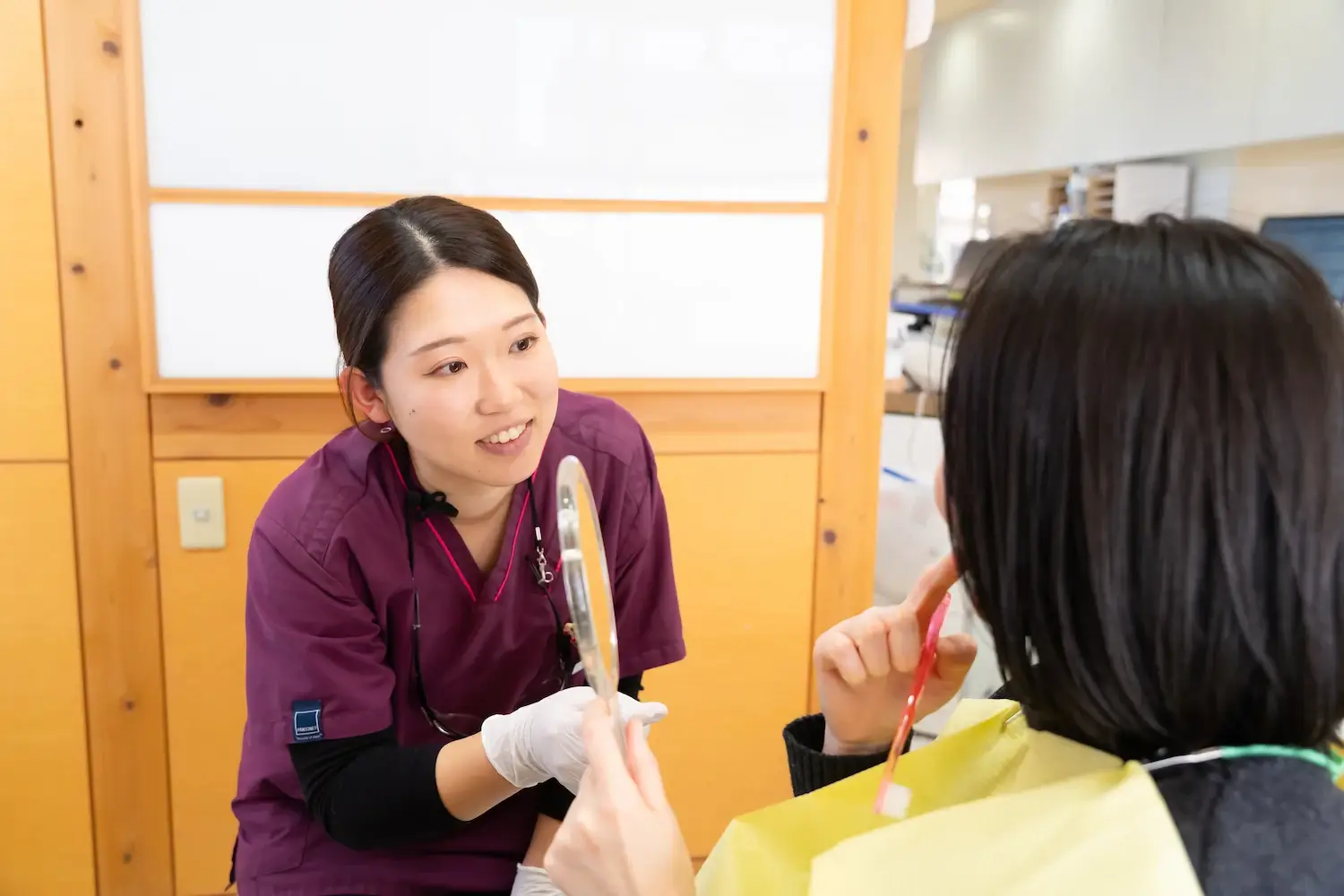 知立市シン歯科クリニックのスタッフと、鏡を見ながら口の中の説明を受けている患者さん